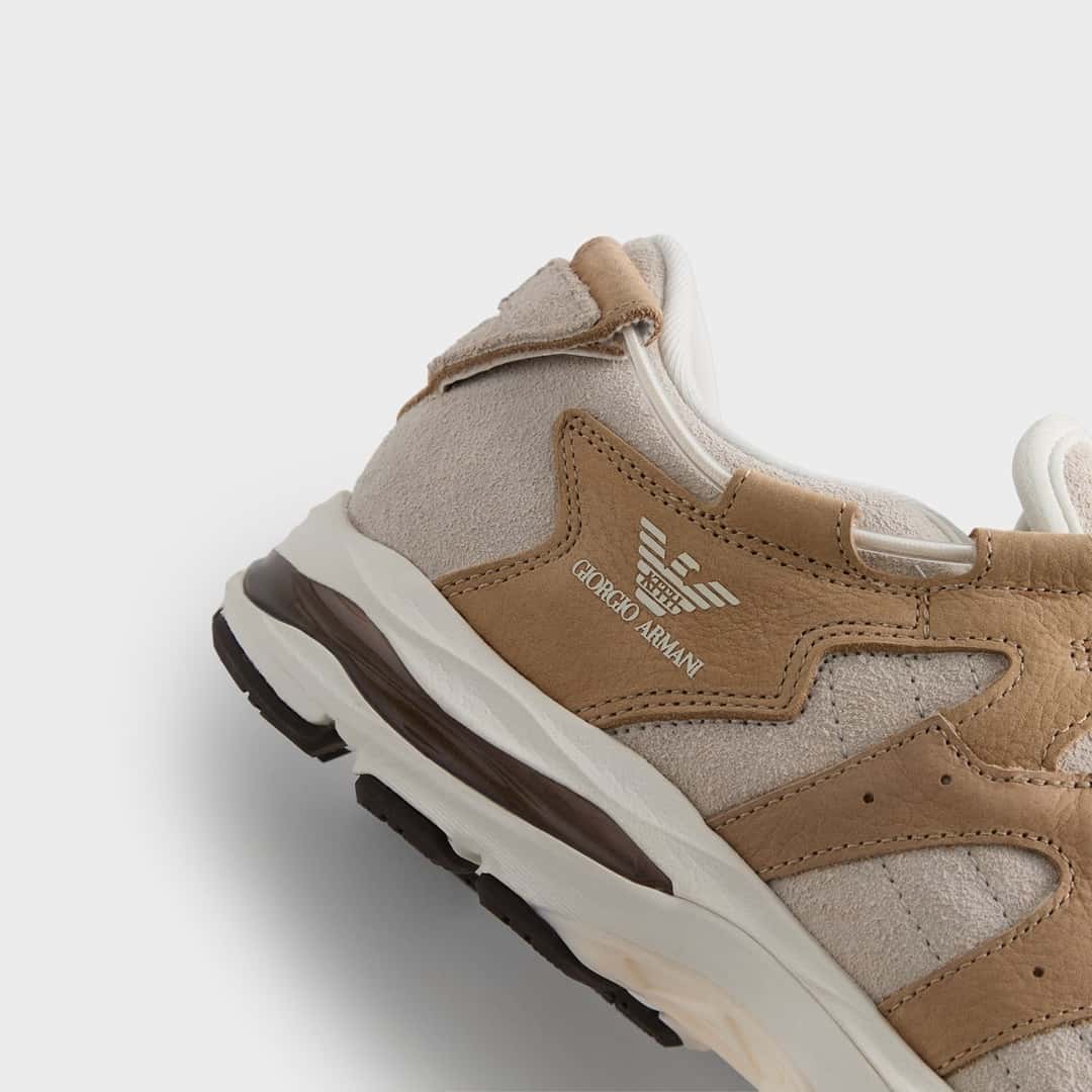 Primer plano de la parte trasera del lateral de la ASICS GEL-MAI 0.1 Safari de Giorgio Armani x Kith sobre fondo gris claro, con el águila de Giorgio Armani y la palabra Kith adentro estampadas sobre nubuck color camel, gamuza clara y mediasuela blanca con detalles marrón oscuro