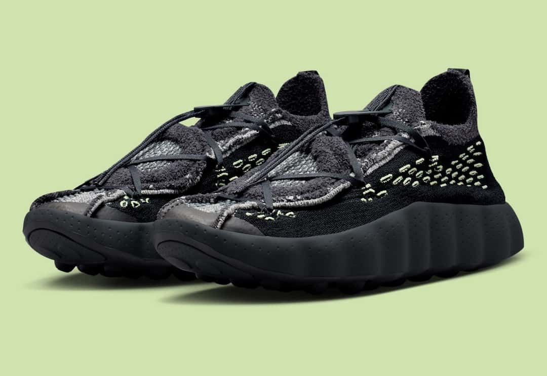 Par de Nike Mind 002 Flyknit Black/Dark Smoke Grey en vista diagonal, con costuras verde lima sobre tejido negro y gris