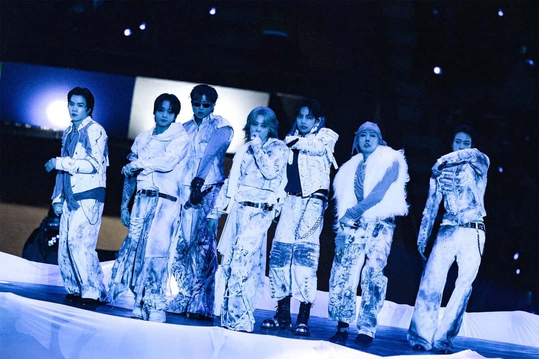 BTS en el escenario del Estadio Único de La Plata con trajes blancos estampados, sobre una plataforma iluminada en azul. Foto: HYBE/BIGHIT MUSIC