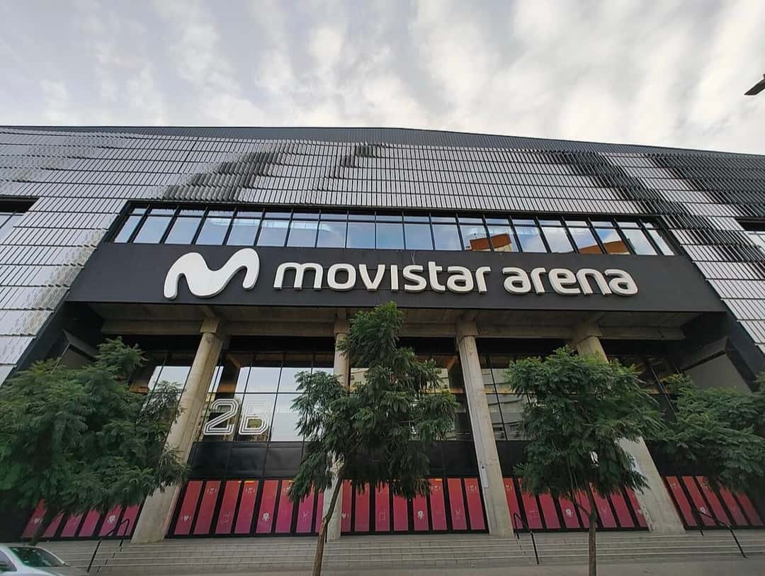 Fachada del Movistar Arena de Buenos Aires, con el cartel del estadio sobre la entrada vidriada y árboles en la vereda. Foto: BugWarp, CC BY-SA 4.0, vía Wikimedia Commons