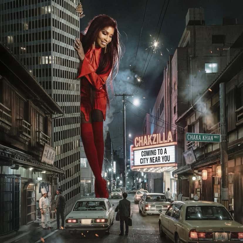 Portada del single «Chakzilla», de Chaka Khan: la cantante, gigante y vestida de rojo, se asoma entre edificios de una calle nocturna con autos antiguos y un cartel de cine