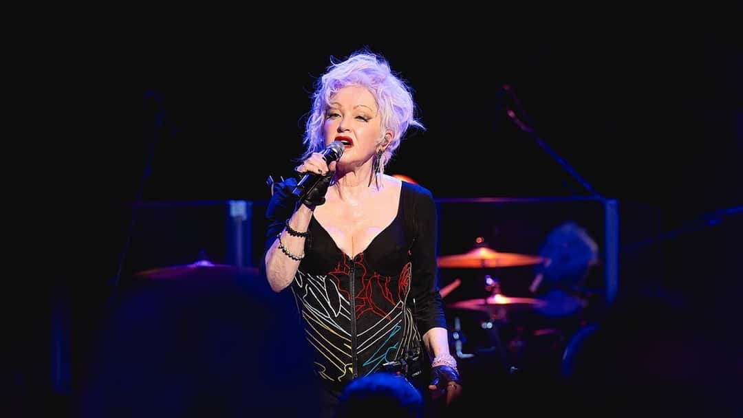 Cyndi Lauper canta con un micrófono en la mano, de pelo platinado y vestido negro, en el Royal Albert Hall de Londres, en 2024. Foto: Raph_PH, CC BY 2.0, vía Wikimedia Commons (foto de archivo)