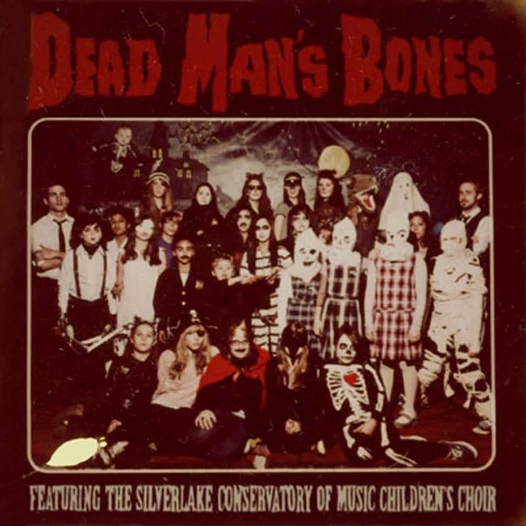 Portada del disco «Dead Man's Bones» de 2009: una foto antigua en sepia de un grupo de chicos y adultos disfrazados de esqueletos, fantasmas y vampiros, con el nombre de la banda en letras rojas arriba y la mención al coro de niños abajo