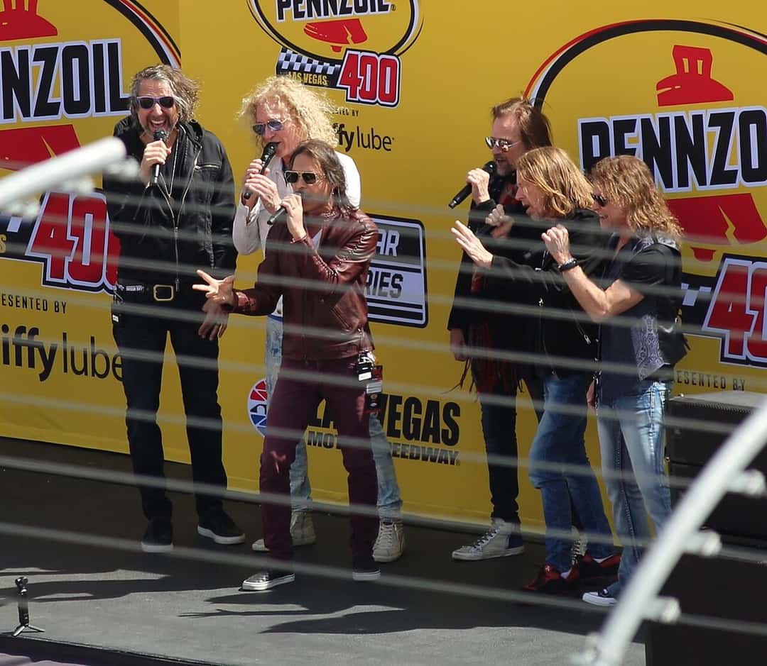 Integrantes de Foreigner cantan el himno de Estados Unidos con micrófonos en mano, frente a un cartel amarillo de una carrera, en el Las Vegas Motor Speedway en marzo de 2026 (foto de archivo). Foto: TaurusEmerald, CC BY-SA 4.0, vía Wikimedia Commons