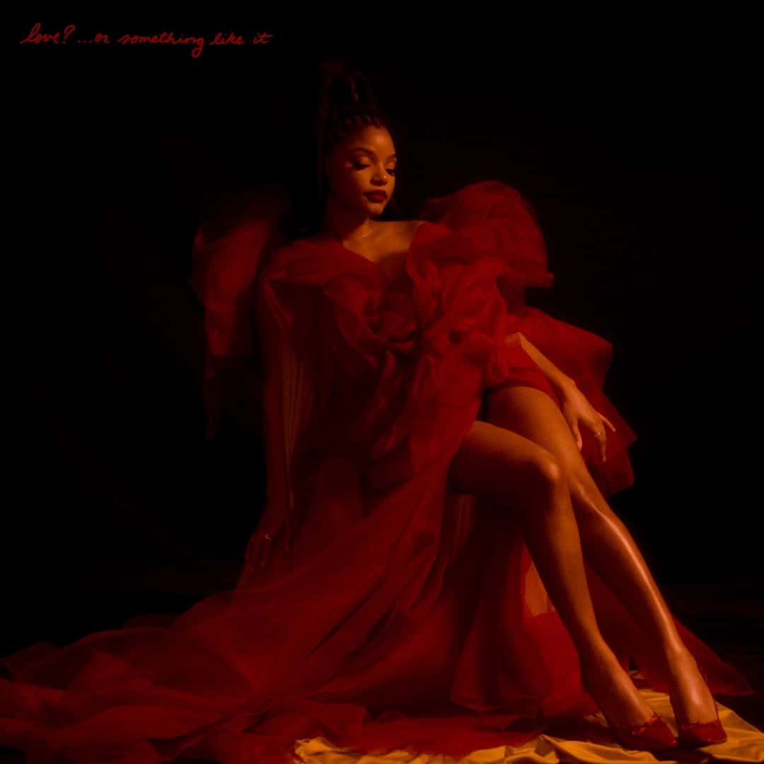 Portada original de «love?... or something like it», de 2025: Halle Bailey sentada con un vestido de volados en tonos rojos sobre fondo negro