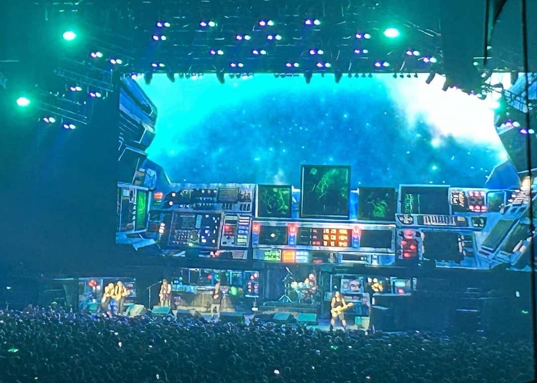 Escenario de la Run For Your Lives World Tour de Iron Maiden en París, el 20 de julio de 2025 (foto de archivo): la pantalla gigante muestra el tablero de una nave espacial, con monitores y luces de colores frente a un cielo estrellado, mientras la banda toca abajo ante una multitud. Foto: Chris93, Wikimedia Commons, CC BY-SA 4.0