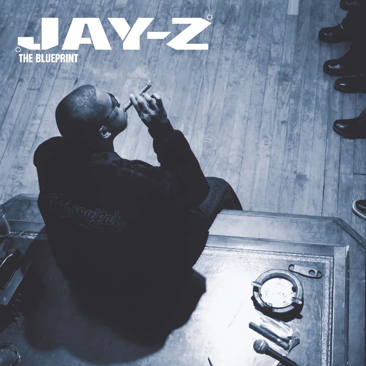 Portada de «The Blueprint», de Jay-Z: el rapero, visto desde arriba, fuma un habano sentado sobre un escritorio, en tonos azules