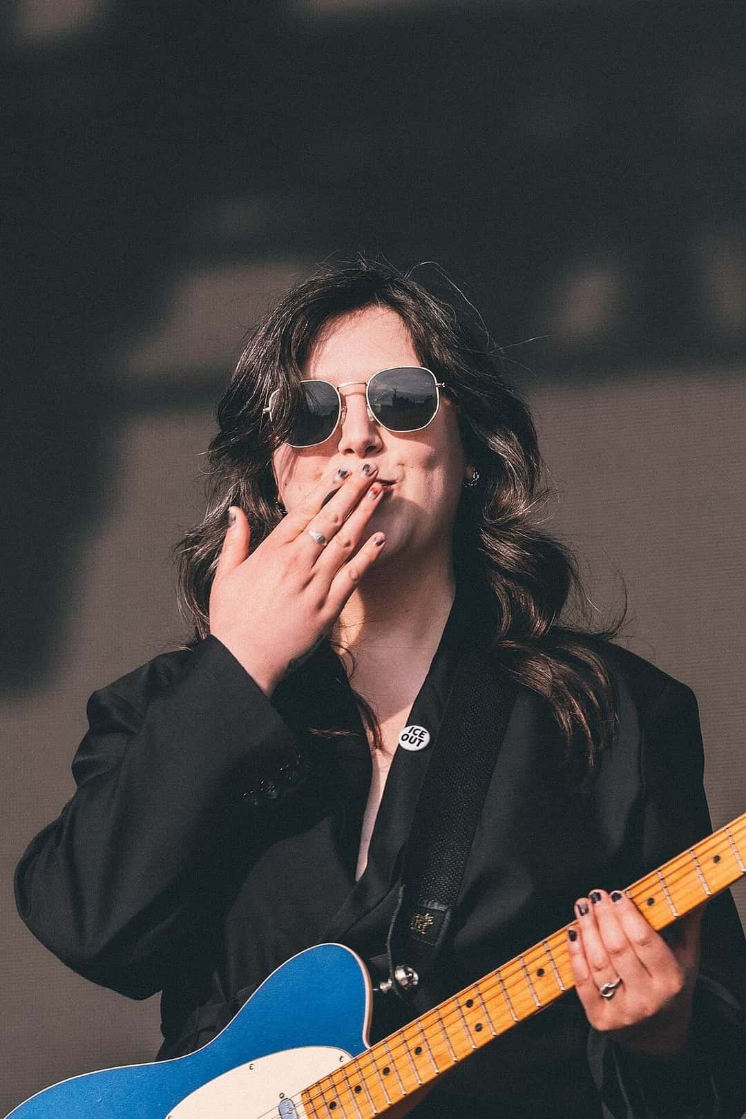 Lucy Dacus, con anteojos de sol y saco negro, toca una guitarra eléctrica azul y tira un beso al público, en la edición 2026 de Kilby Block Party (foto de archivo). Foto: Anson Tong, CC BY-SA 4.0, vía Wikimedia Commons
