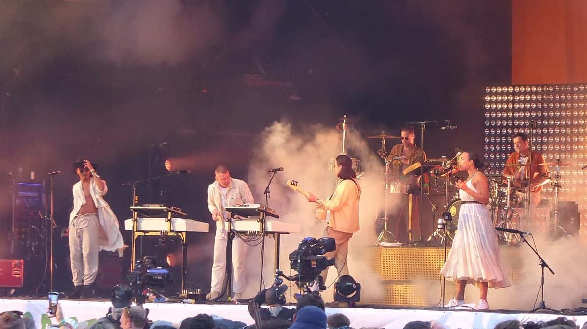 Jungle toca en vivo en un escenario de festival lleno de humo, con los músicos vestidos de blanco y beige entre teclados, guitarras y una batería, en junio de 2019 (foto de archivo)