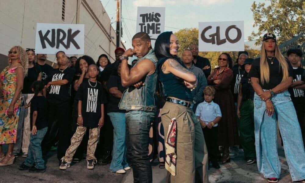 Foto de prensa de «This Time»: Kirk Franklin, con chaleco de jean, y GloRilla, de remera negra y pantalón cargo, espalda con espalda en una calle de barrio, rodeados de gente con remeras negras y carteles que dicen KIRK, THIS TIME y GLO