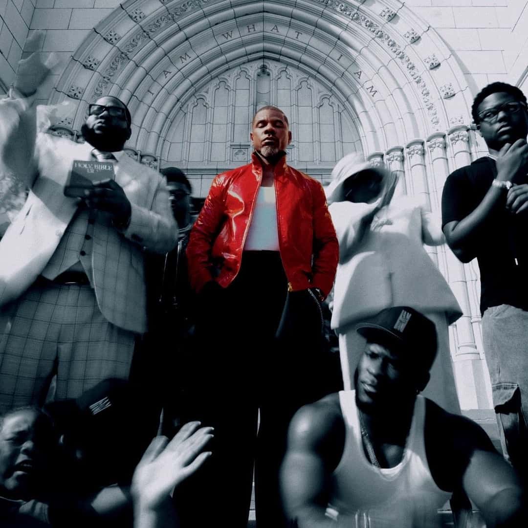 Portada oficial de «I Am What I Am»: Kirk Franklin, con campera de cuero roja y remera blanca, en el centro de la escalinata de una iglesia de piedra con arcos tallados, rodeado de personas en blanco y negro, una con una Biblia y otra con las manos en alto. Imagen: Uptown Records / Fo Yo Soul