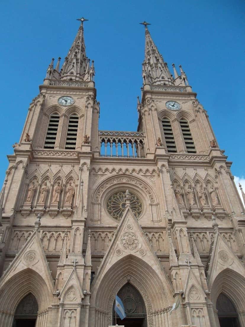 Fachada de piedra de la Basílica de Nuestra Señora de Luján, con sus dos torres en punta, vista desde abajo contra el cielo celeste (foto de archivo). Foto: Federico Gomez Aghetta, dominio público, vía Wikimedia Commons