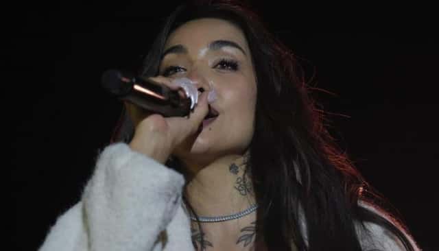 María Becerra cantando con micrófono en mano y un abrigo blanco de piel, durante una presentación de