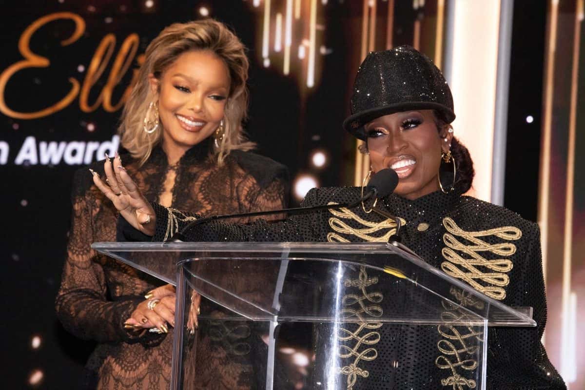 Missy Elliott, con gorra y chaqueta negras bordadas en dorado, habla en un atril de acrílico mientras Janet Jackson, con vestido de encaje, la aplaude a su lado en el escenario de la Gala of the Stars