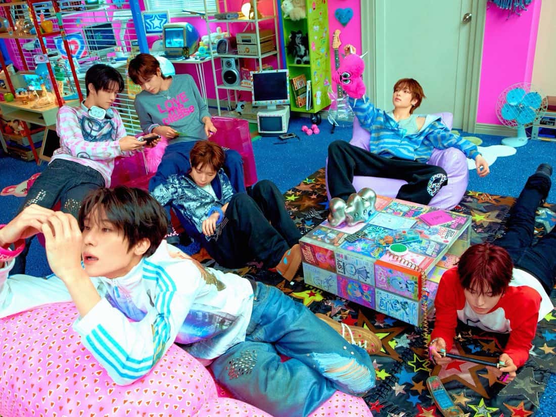 Foto oficial de NCT WISH para "I SPY": los seis integrantes tirados en almohadones y sillones inflables en un cuarto rosa lleno de juguetes, monitores viejos y una alfombra con estrellas