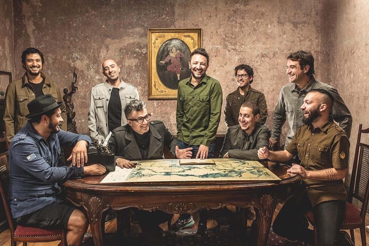 No Te Va Gustar en una sesión de fotos de 2017: los integrantes de la banda, sonrientes, alrededor de una mesa de madera con un mapa antiguo, en una sala con paredes gastadas y un cuadro de marco dorado (foto de archivo)