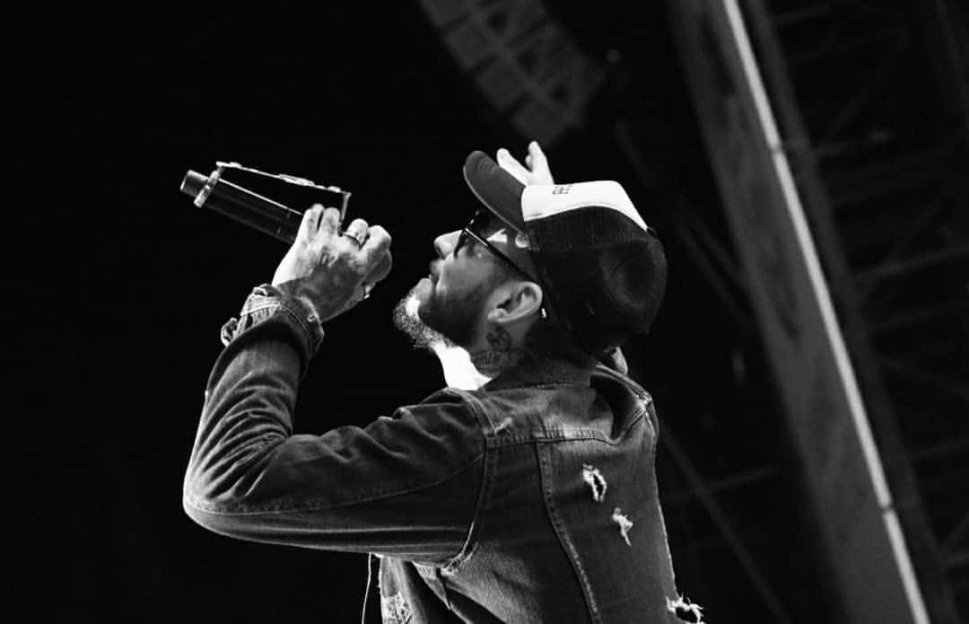Ulises Bueno canta con gorra, anteojos y campera de jean, con el micrófono en alto, en una foto en blanco y negro de un show (foto de archivo, 2019). Foto: Ulises Bueno Oficial, CC BY-SA 4.0, vía Wikimedia Commons