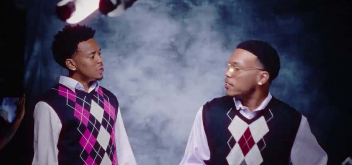 Fotograma del visualizer oficial de «Days Go By»: Cordae y Anderson .Paak, con chalecos de rombos rosa y bordó sobre camisas claras, se miran de reojo frente a un fondo de humo azul