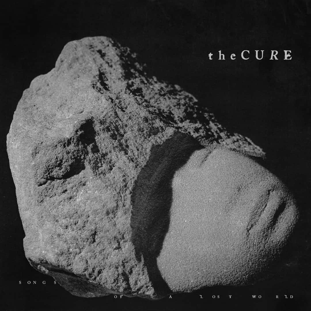 Portada de «Songs of a Lost World», el disco de The Cure de 2024: una escultura de piedra gris con forma de rostro sobre fondo negro, con el nombre del grupo arriba a la derecha