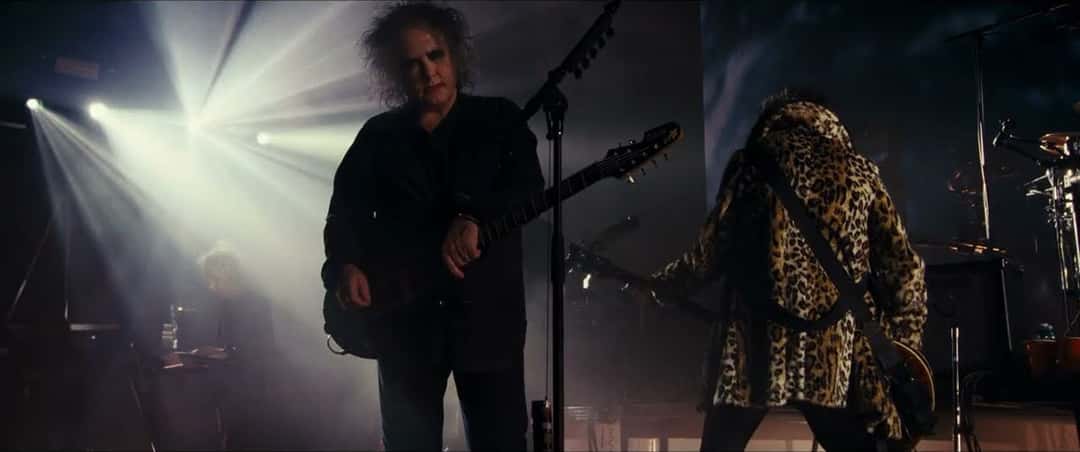 Fotograma del video oficial de The Cure en el Troxy de Londres en 2024: Robert Smith toca la guitarra bajo luces blancas, junto a un músico con abrigo de leopardo (foto de archivo)