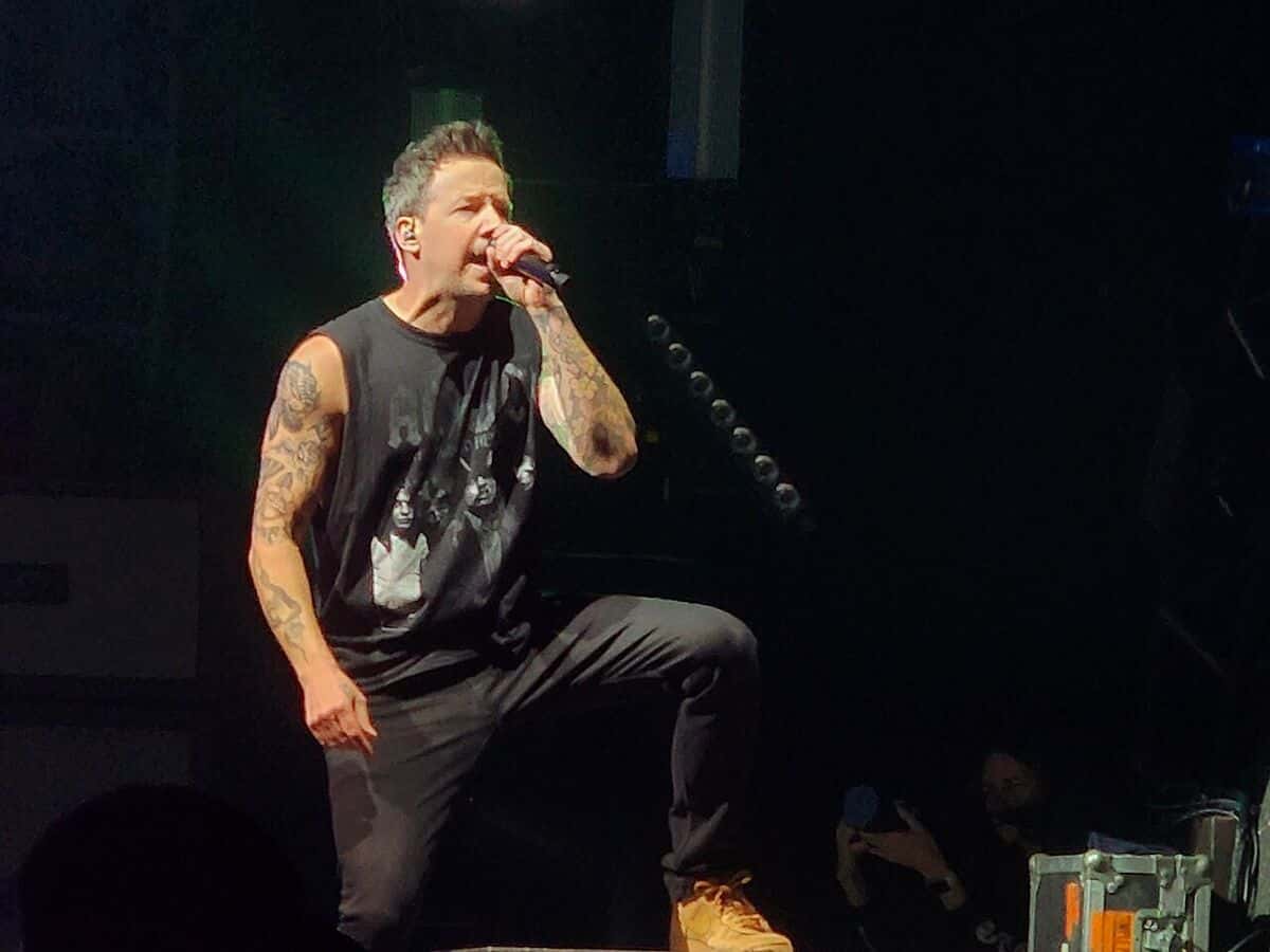 Pierre Bouvier, cantante de Simple Plan, canta con el micrófono en la mano y una musculosa negra, apoyado en un monitor de un escenario oscuro, en noviembre de 2022 (foto de archivo)