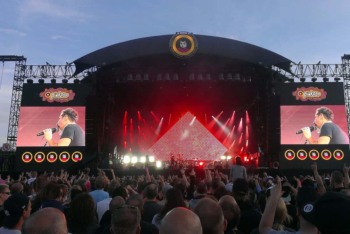 System of a Down en vivo en el festival Pinkpop 2017 (foto de archivo): escenario con luces rojas, pantallas a los costados con el cantante y el público en primer plano