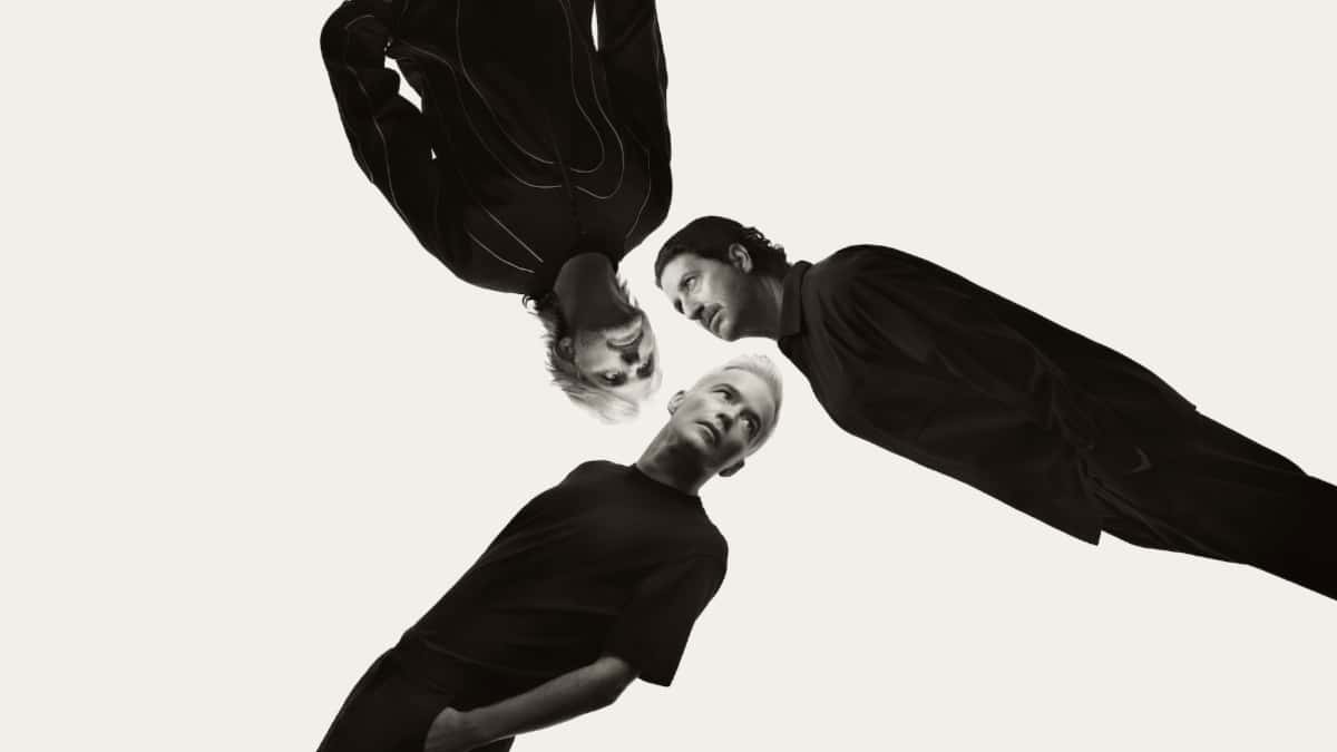 Foto de prensa en blanco y negro de The Avalanches: tres integrantes vestidos de negro, uno cabeza abajo, que se miran entre sí contra un fondo claro