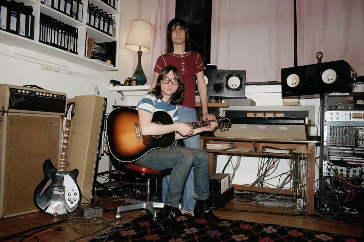 Los hermanos Brian y Michael D'Addario de The Lemon Twigs en su estudio: uno sentado con anteojos y una guitarra acústica sunburst, el otro parado detrás con remera roja, entre amplificadores, monitores y una guitarra eléctrica apoyada