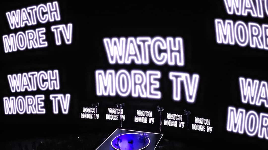 U2 en la Sphere de Las Vegas en octubre de 2023: pantallas gigantes con la frase «WATCH MORE TV» repetida en letras blancas sobre fondo negro, y el escenario circular iluminado de violeta abajo (foto de archivo). Foto: Dave Stadley, CC BY-SA 4.0, vía Wikimedia Commons