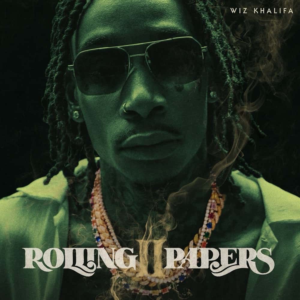 Portada de «Rolling Papers 2», de Wiz Khalifa: primer plano del rapper con anteojos de sol, rastas y collares, bañado en luz verde y humo
