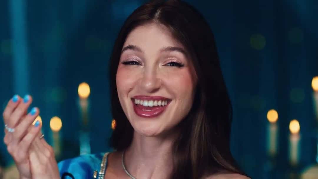 Yami Safdie, de pelo largo castaño, se ríe frente a la cámara con las uñas pintadas de celeste, en una fiesta con velas de fondo, en una imagen del video oficial de «Felicidades»