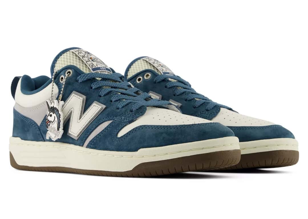 Par del Focus x New Balance Numeric 480 sobre fondo blanco, con gamuza azul petróleo, cuero blanco en talón y punta, N blanca con borde gris, plaquita colgante con un unicornio y logo de Focus en la lengüeta, sobre suela crema con base color goma