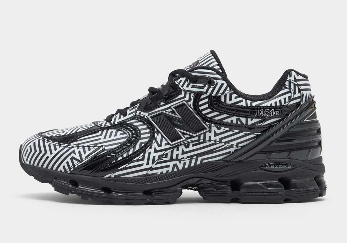 New Balance 1954R Dazzle Camo de perfil sobre fondo gris claro, con estampado de líneas blancas y negras en toda la capellada, logo N negro y entresuela negra