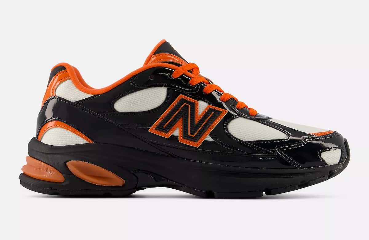 Vista lateral externa del New Balance 2010 Halloween sobre fondo gris claro, con capellada de charol negro brillante, paneles de malla crema, logo N negro con borde naranja, cordones y cuello naranjas y pods de amortiguación naranjas en el talón sobre la suela negra
