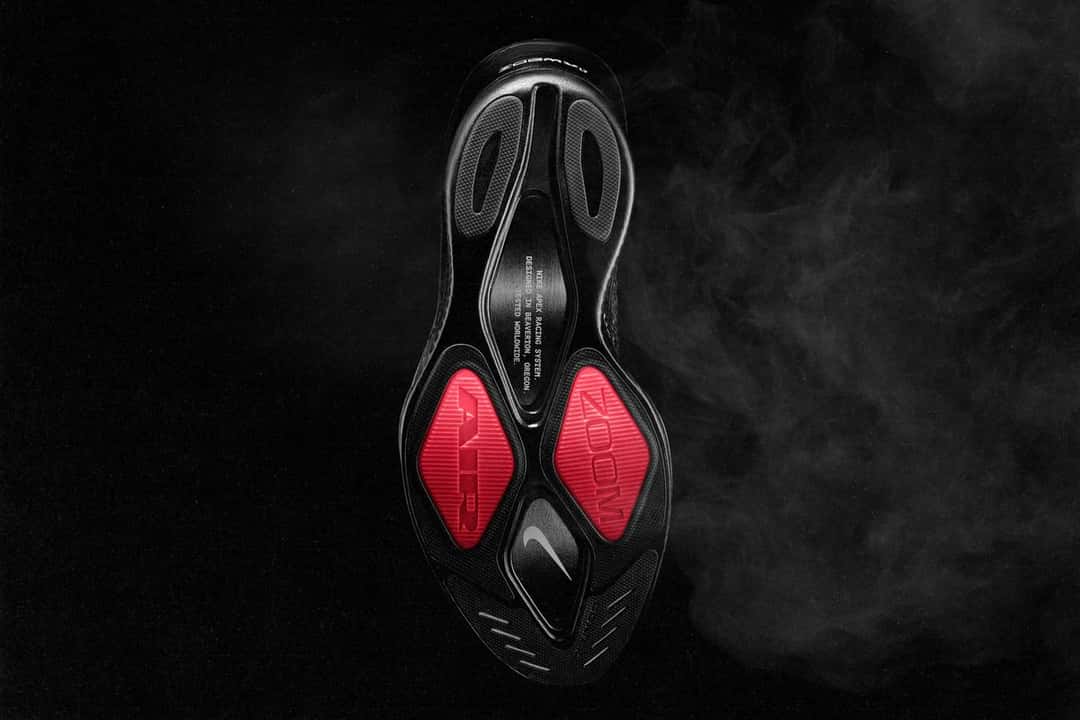 Suela de la Nike Apex negra vista desde abajo, con dos rombos de goma roja que dicen AIR y ZOOM bajo el antepié, un Swoosh en el medio y la inscripción Nike Apex Racing System en el arco