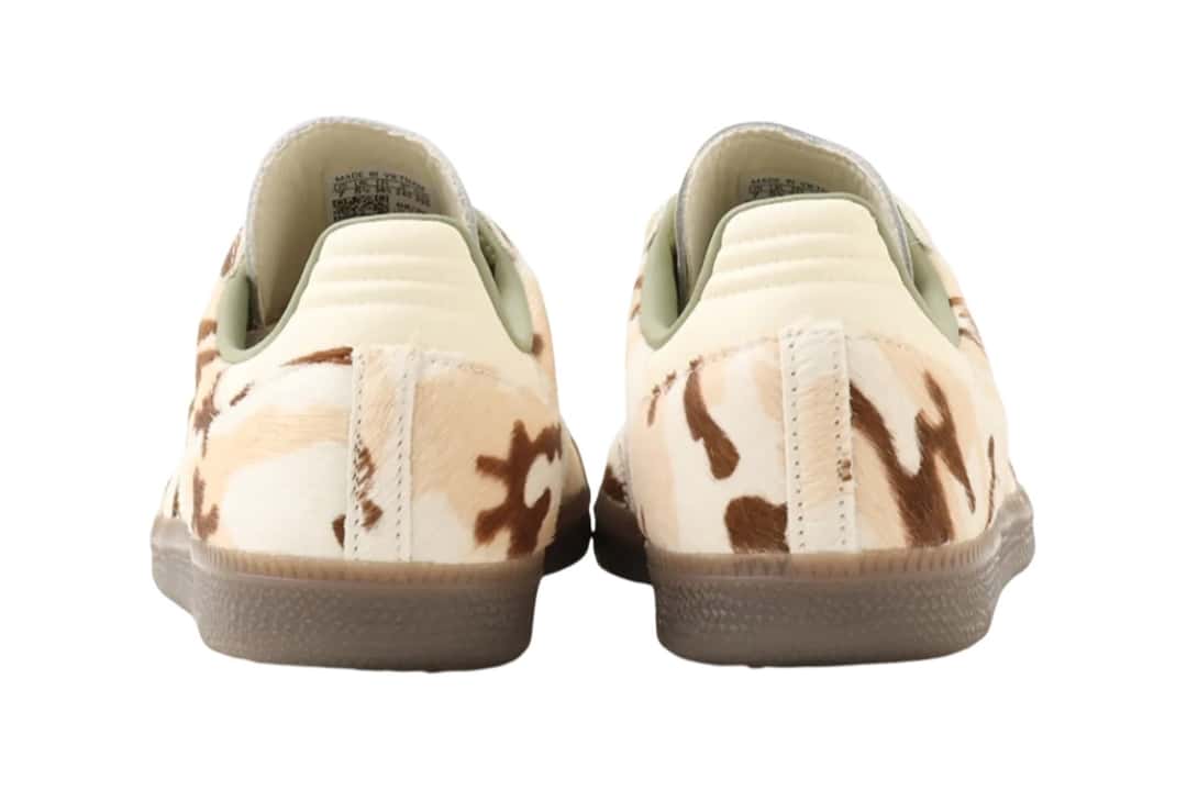 Vista trasera del par de adidas Samba Camo Cow Print, con los talones de cuero crema acolchados, el forro verde salvia, el pelo con manchas marrones y beige en los laterales y la suela gum oscura