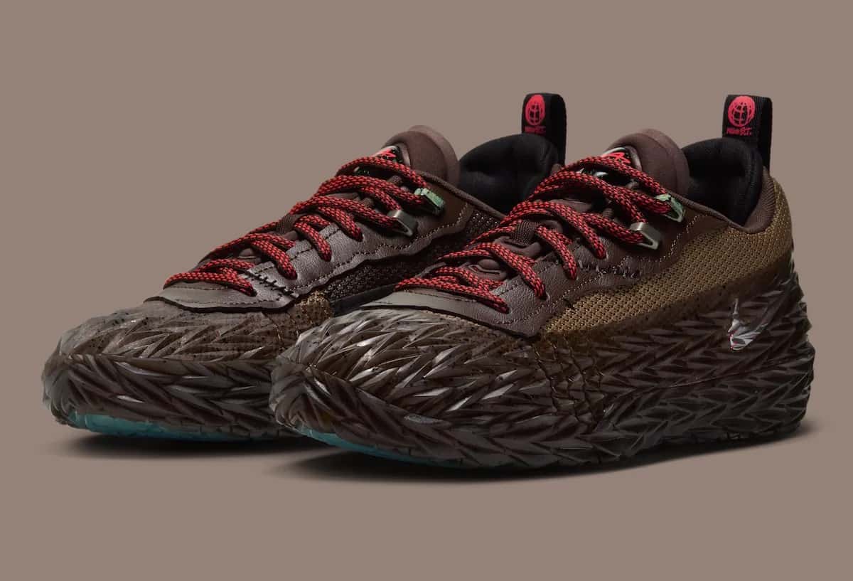 Par de Nike ST Charge Halloween de Cade Cunningham sobre fondo marrón grisáceo, con la capa de goma texturada con púas en marrón oscuro, paneles de malla tostada, cuero marrón en el sector de los cordones, cordones rojos con negro y tiradores negros con el logo Nike S.T. en rojo