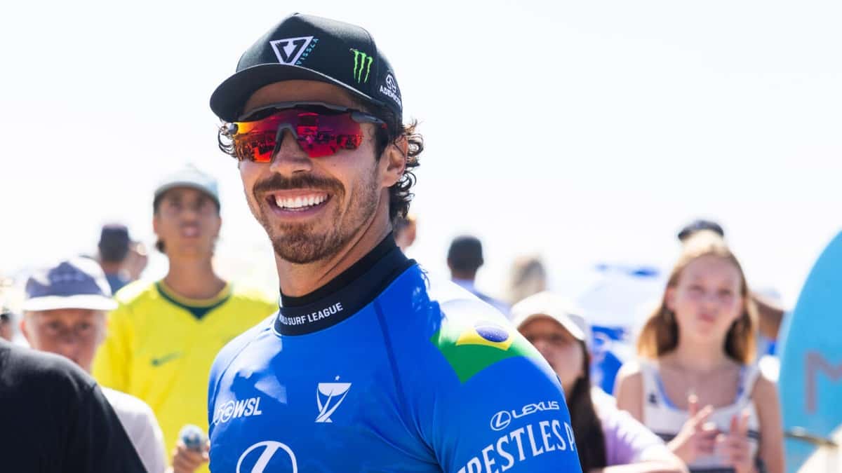 Foto de archivo: Yago Dora sonríe con gorra negra, anteojos espejados y la lycra azul de la WSL con la bandera de Brasil en Trestles 2026