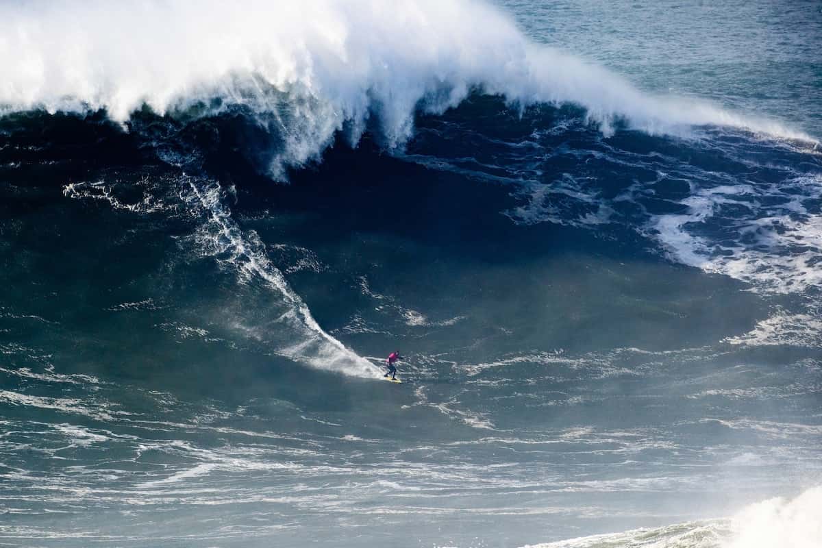 Foto de archivo: Nic von Rupp, con traje rosa, baja una ola gigante en Praia do Norte durante el Nazaré Big Wave Challenge del 13 de diciembre de 2025, con la espuma rompiendo detrás