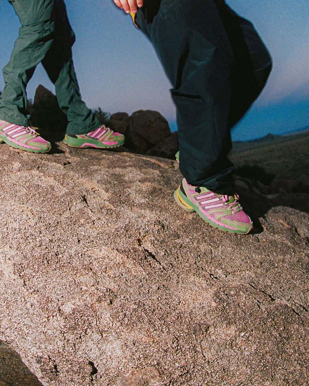 Dos personas paradas sobre una roca con la The Tipping Point x adidas Adistar Control 5 rosa y verde puesta