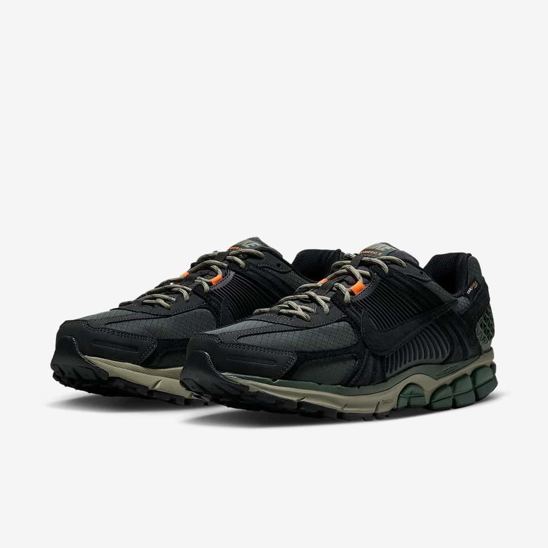 Par de Nike Zoom Vomero 5 Cordura Camo Green en vista diagonal, con capellada negra, detalles verdes y naranjas y entresuela verde oliva