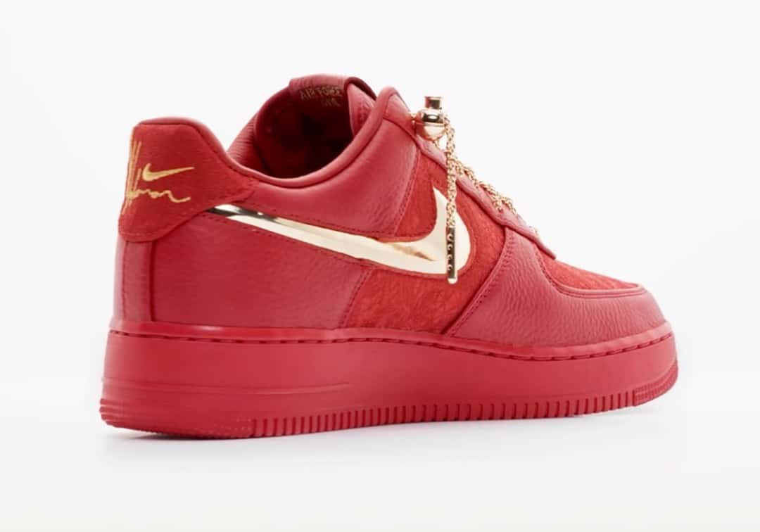 Talón del Victor Solomon x Nike Air Force 1 Low Trophies rojo sobre fondo blanco, con la firma del artista bordada en dorado, el Swoosh metálico y los cordones de soga con el dije colgando
